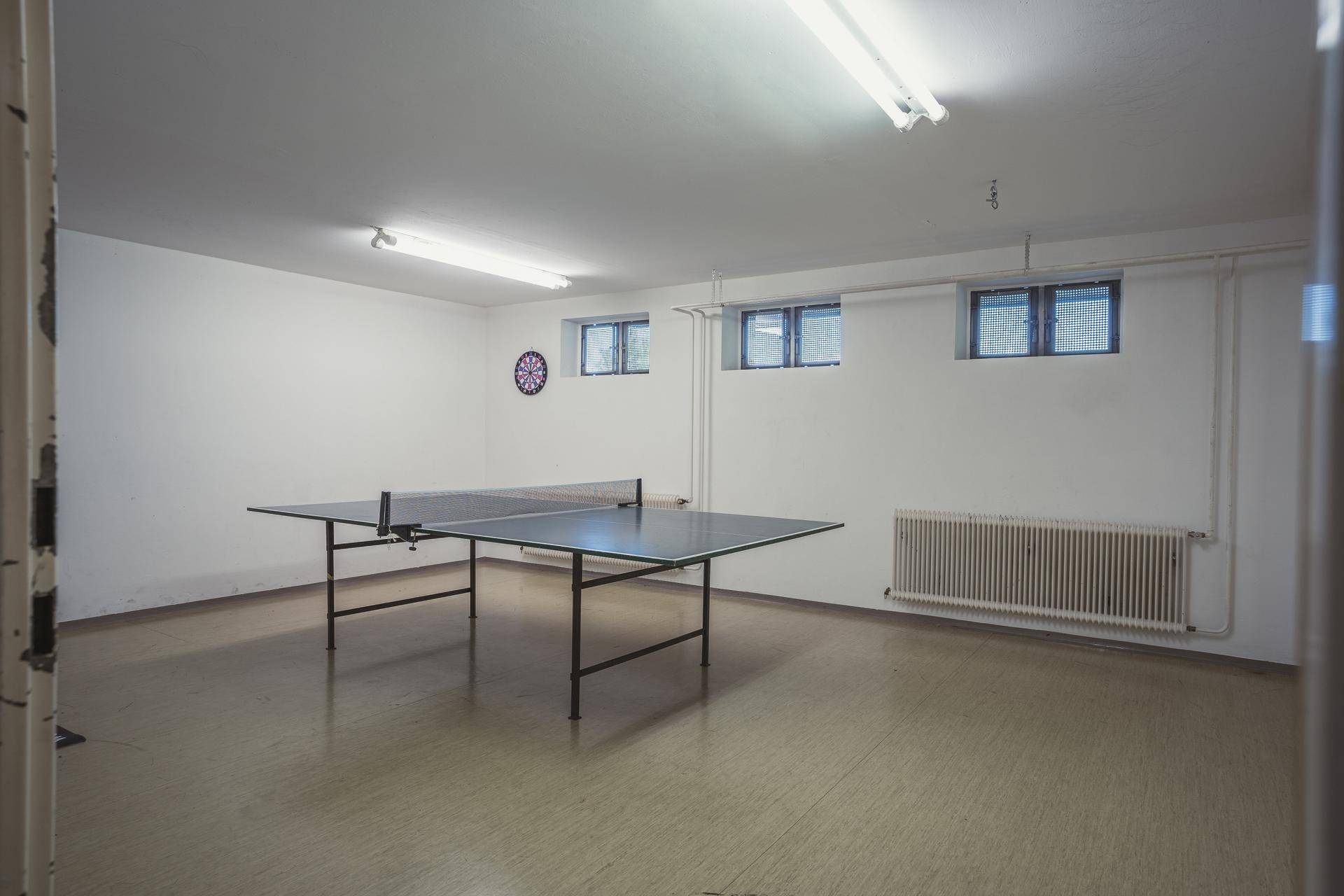 Geräumiger Hobbyraum im Untergeschoss mit Tischtennisplatte und kleinen Fenstern.