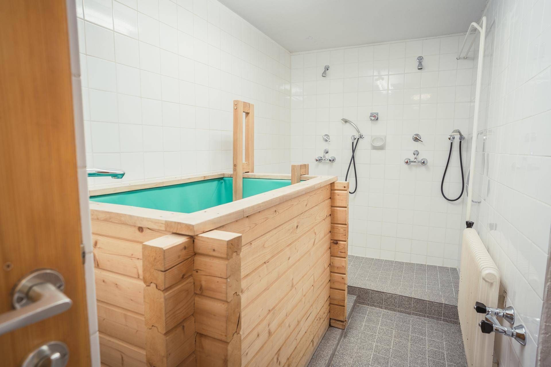 Duschbereich mit mehreren Brausen und einem hölzernen Tauchbecken für Abkühlung.
