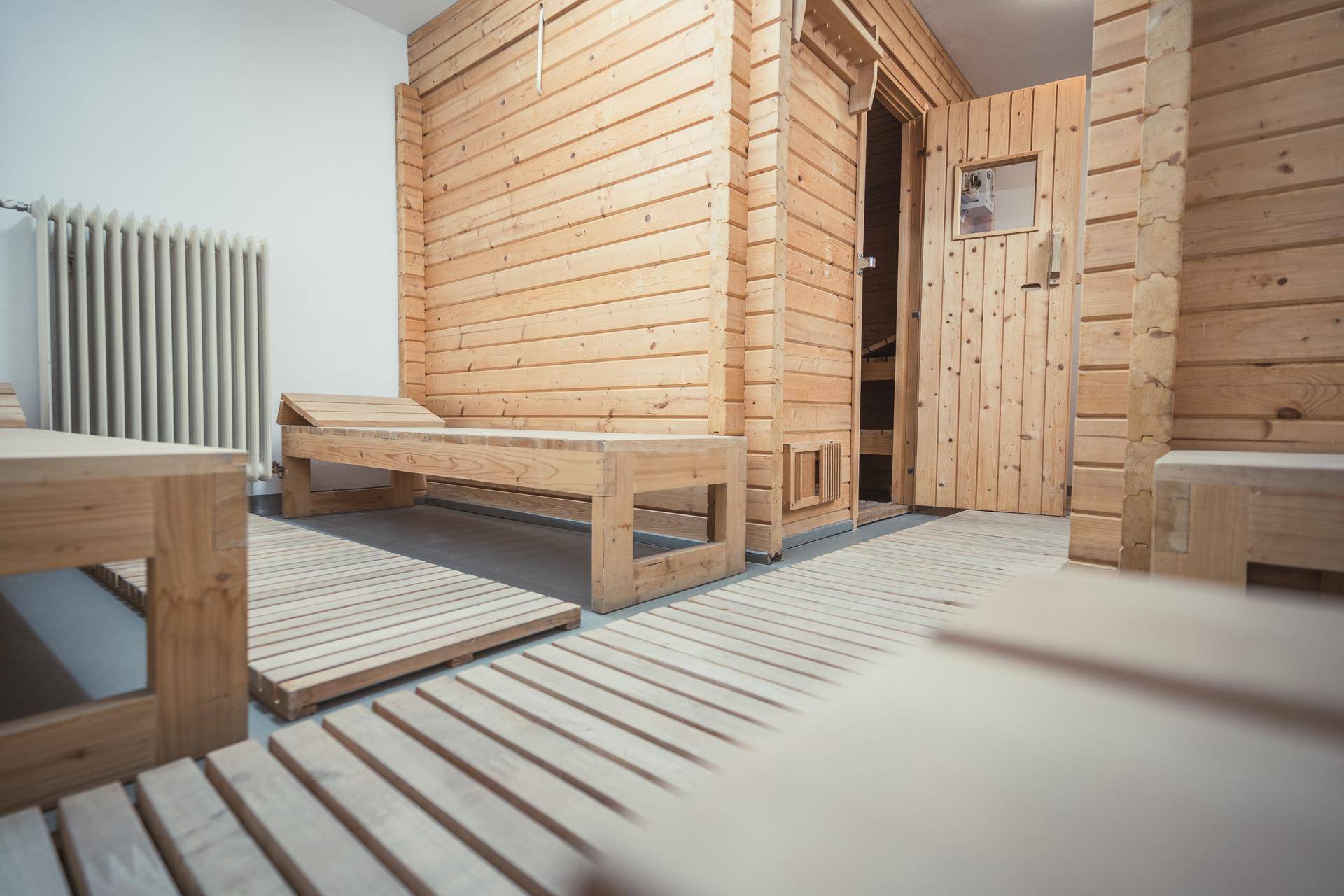 Entspannungsbereich vor der Sauna mit Holzbänken und Lattenrosten auf dem Boden.