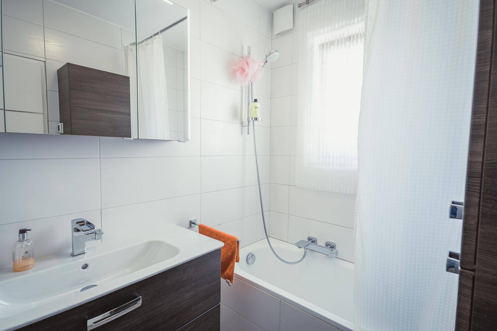 Helles Badezimmer mit Badewanne, Duscharmatur und einem Fenster für Tageslicht.