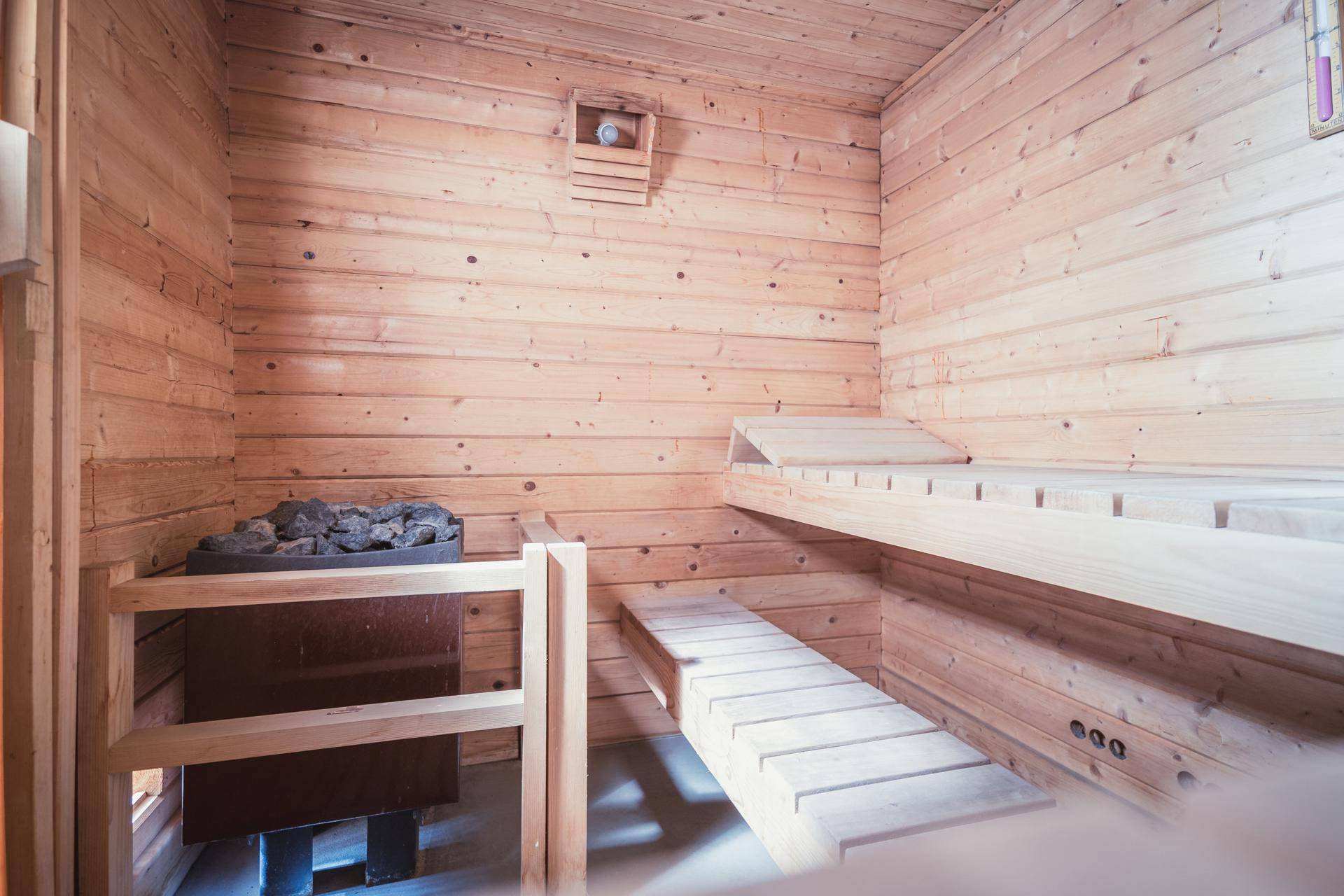 Innenansicht einer traditionellen Holzsauna mit Sitzbänken und einem Saunaofen.