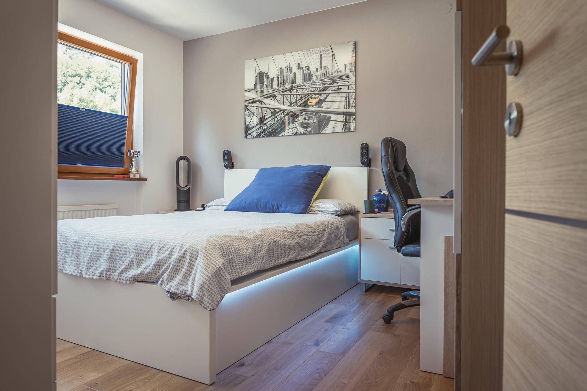 Jugendzimmer mit modernem Bett, Schreibtisch und Blick ins Grüne durch das Fenster.