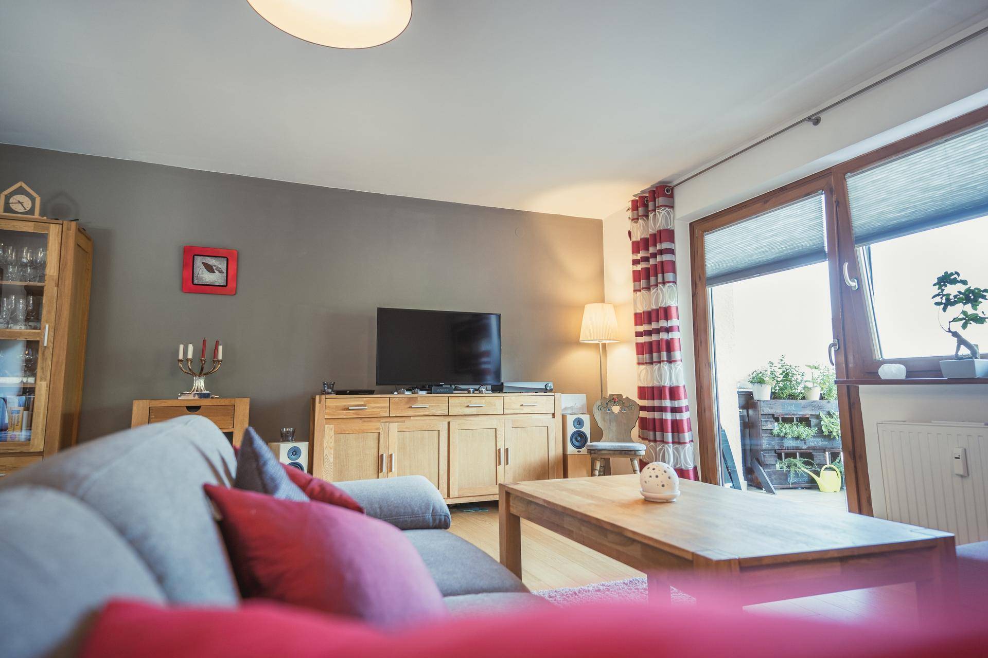 Wohnzimmer mit TV-Möbeln aus Holz, gemütlicher Couch und Zugang zum Balkon.