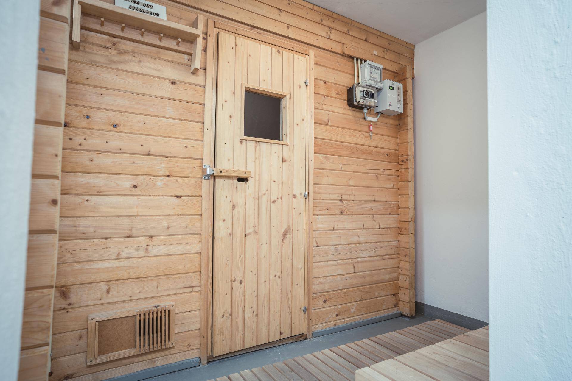 Eingangsbereich zu einer Sauna mit holzverkleideten Wänden und einer Holztür.