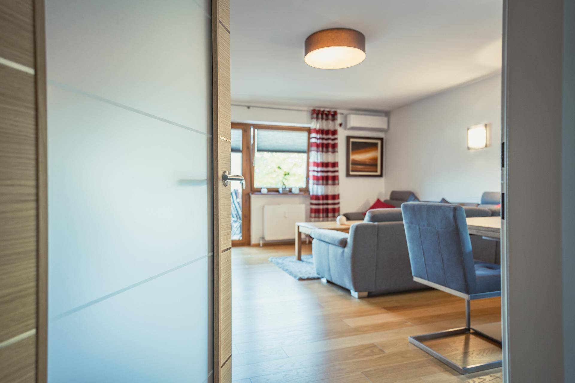 Blick durch eine moderne Glastür in den hellen Wohn-Essbereich mit Holzboden.