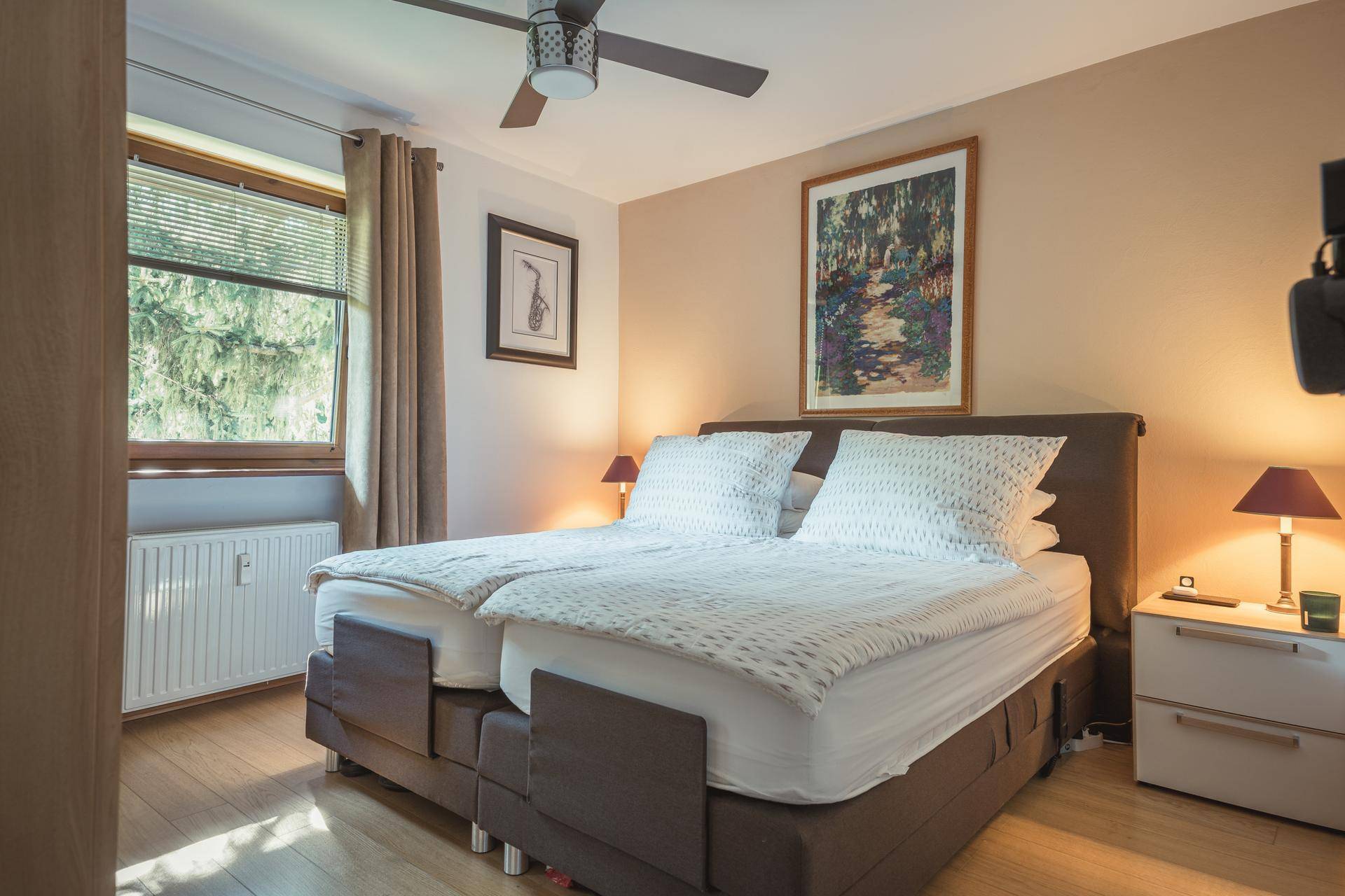 Gemütliches Schlafzimmer mit Doppelbett, Holzboden und Blick ins Grüne durch das Fenster.