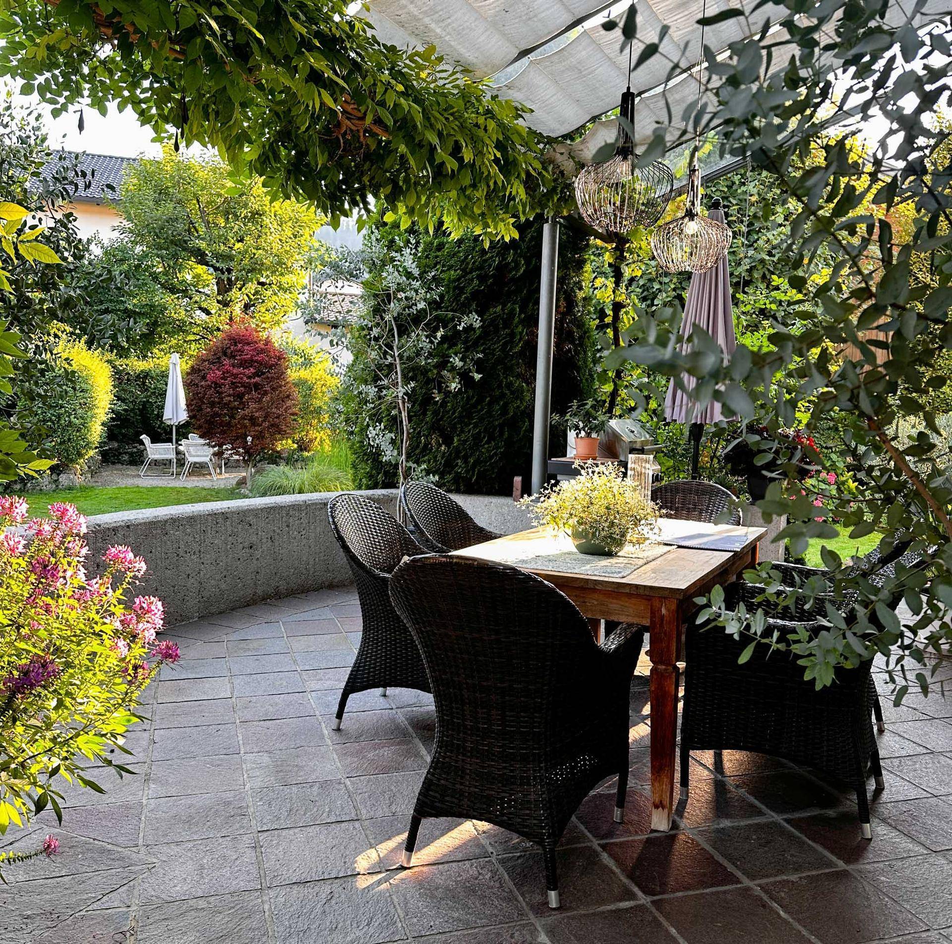 Gemütliche Terrasse mit Esstisch und Stühlen, umgeben von üppigem Grün und Pflanzen.