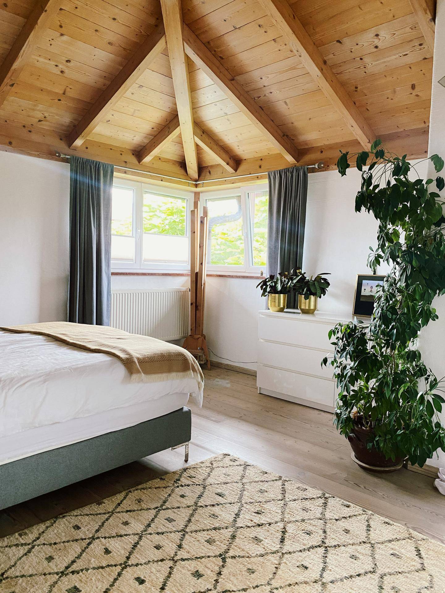 Helles Schlafzimmer mit Holzdachschrägen, großen Fenstern und gemütlicher Atmosphäre.