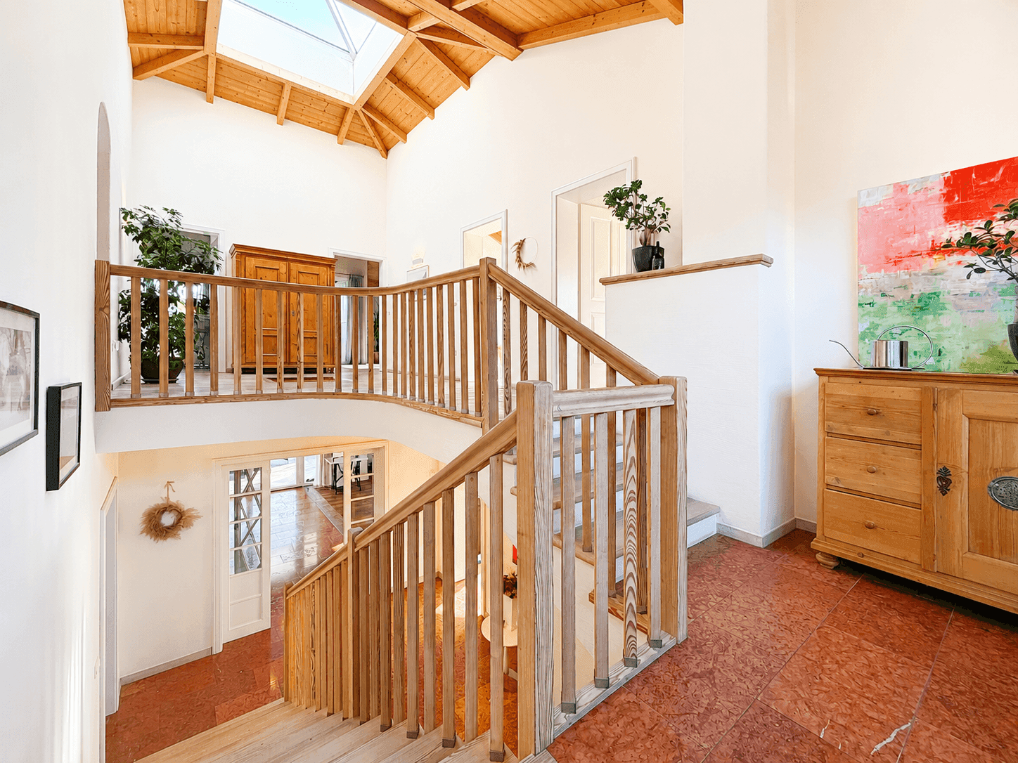 Heller Eingangsbereich mit offener Holztreppe, hohen Decken und großem Oberlicht für viel Tageslicht.