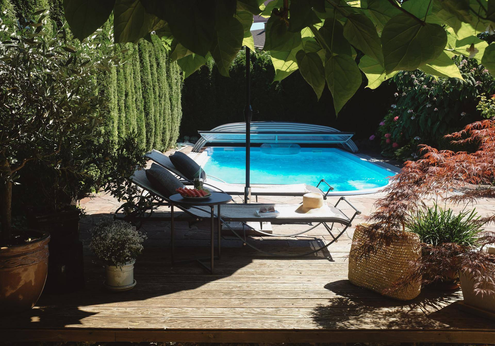 Entspannungsbereich im Garten mit Holzdeck, Liegestühlen und Blick auf den Pool.