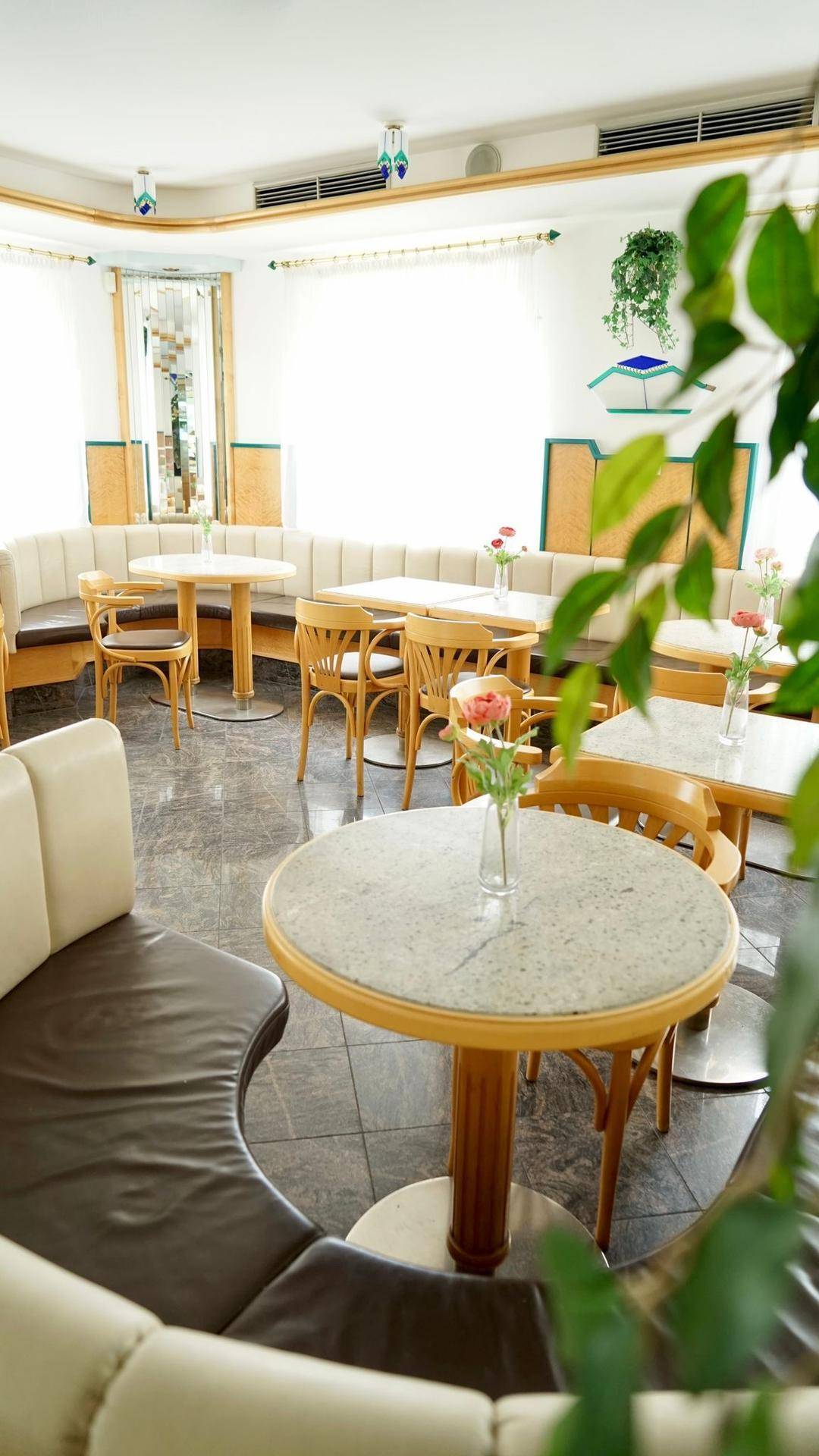 Gemütlicher Café-Sitzbereich mit runden Tischen, bequemen Polsterbänken und natürlichem Licht.