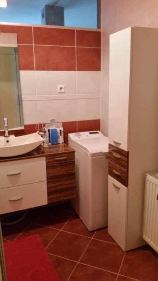 Badezimmer mit Waschbecken, Waschmaschine und praktischem Hochschrank, gefliest in Rot und Weiß.