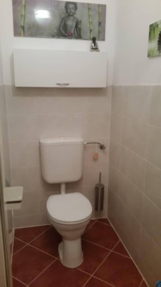 Separates WC mit Toilette, Hängeschrank und gefliesten Wänden und Boden.