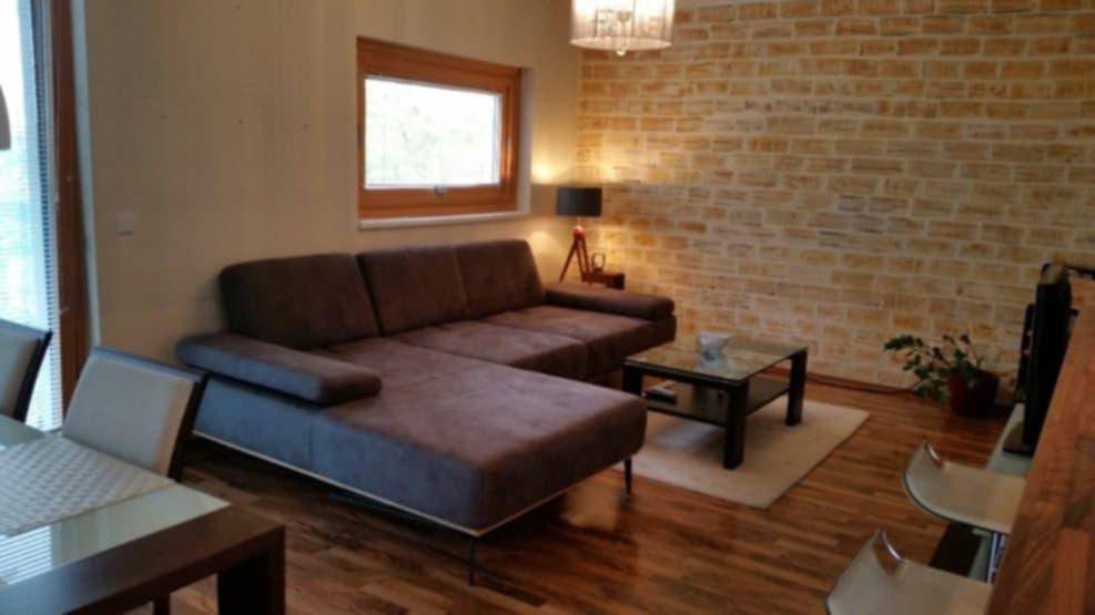 Gemütliches Wohnzimmer mit beiger Ziegelwand, Holzboden und modernem Sofa, hell durch Fenster.