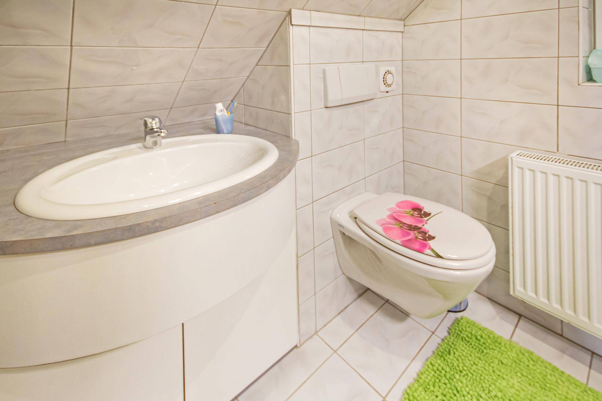Kleines Badezimmer mit Fliesenboden, Waschbecken und WC unter einer Dachschräge.