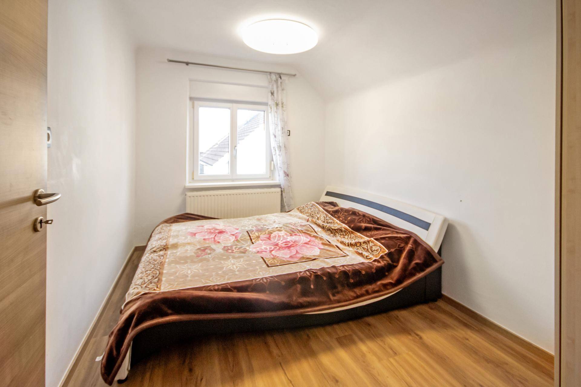 Gemütliches Schlafzimmer mit Bett, Holzboden und Fenster für Tageslicht.