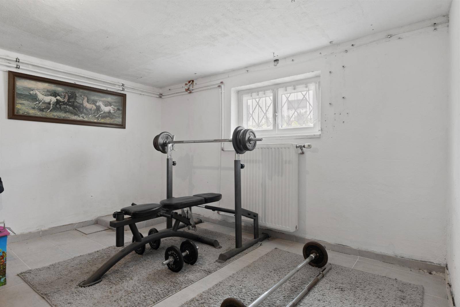 Fitnessbereich im Keller mit Hantelbank und Gewichten für das Training.