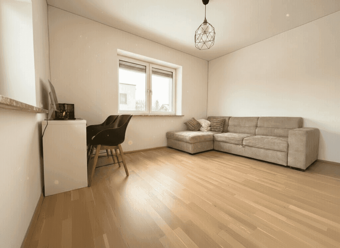 Gemütliches Zimmer mit Parkettboden, Sofa und Schreibtisch am Fenster.