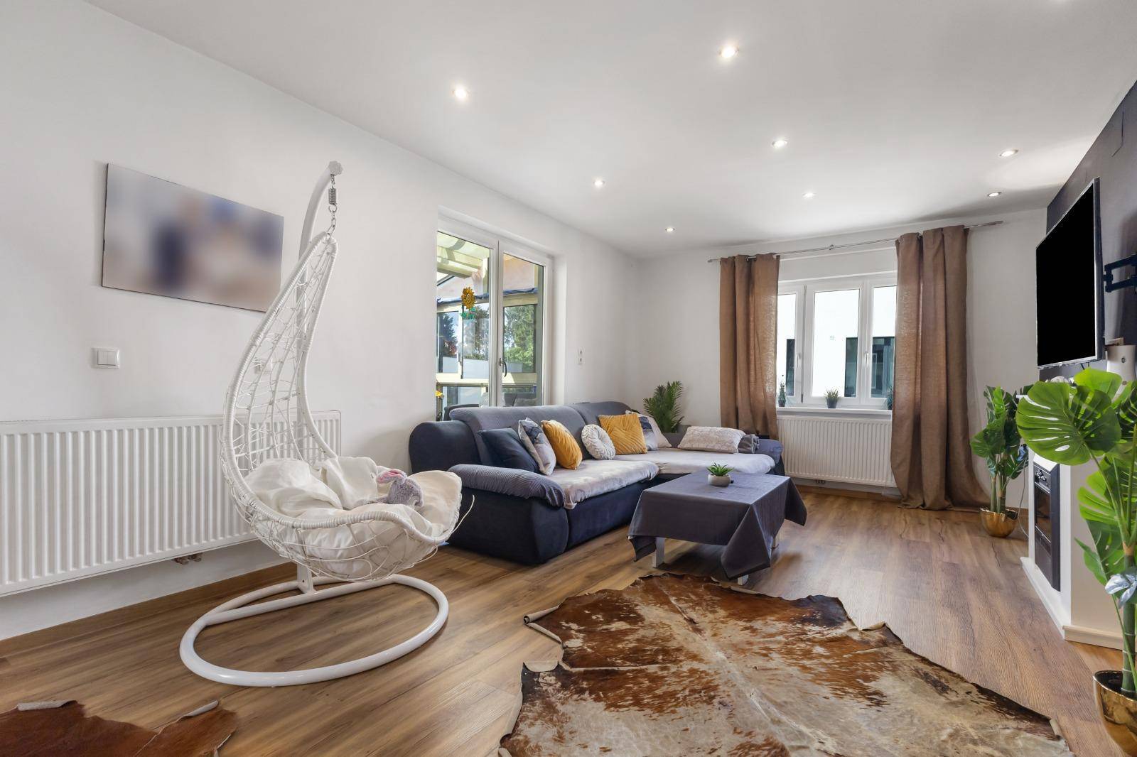 Geräumiges Wohnzimmer mit gemütlichem Sofa, Schaukelstuhl und großen Fenstern für viel Tageslicht.