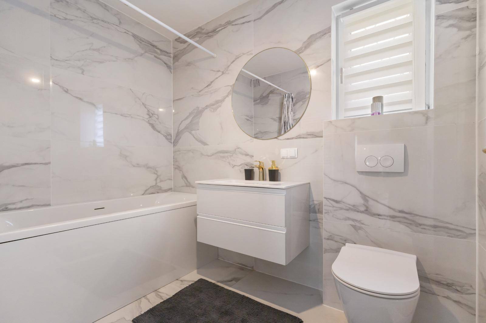 Modernes Badezimmer mit Marmoroptik-Fliesen, Badewanne, schwebendem Waschtisch und Wand-WC.