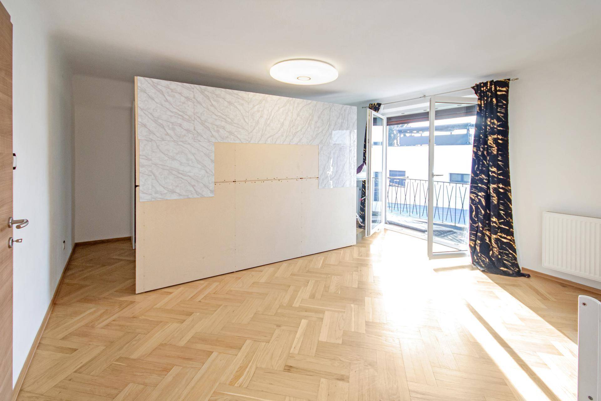 Helles Zimmer mit Fischgrätparkett, großem Fenster und Zugang zu einem französischen Balkon.
