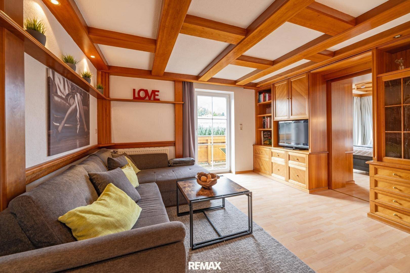 Geräumiges Wohnzimmer mit Holzbalkendecke, Einbauschränken und Zugang zum Balkon.
