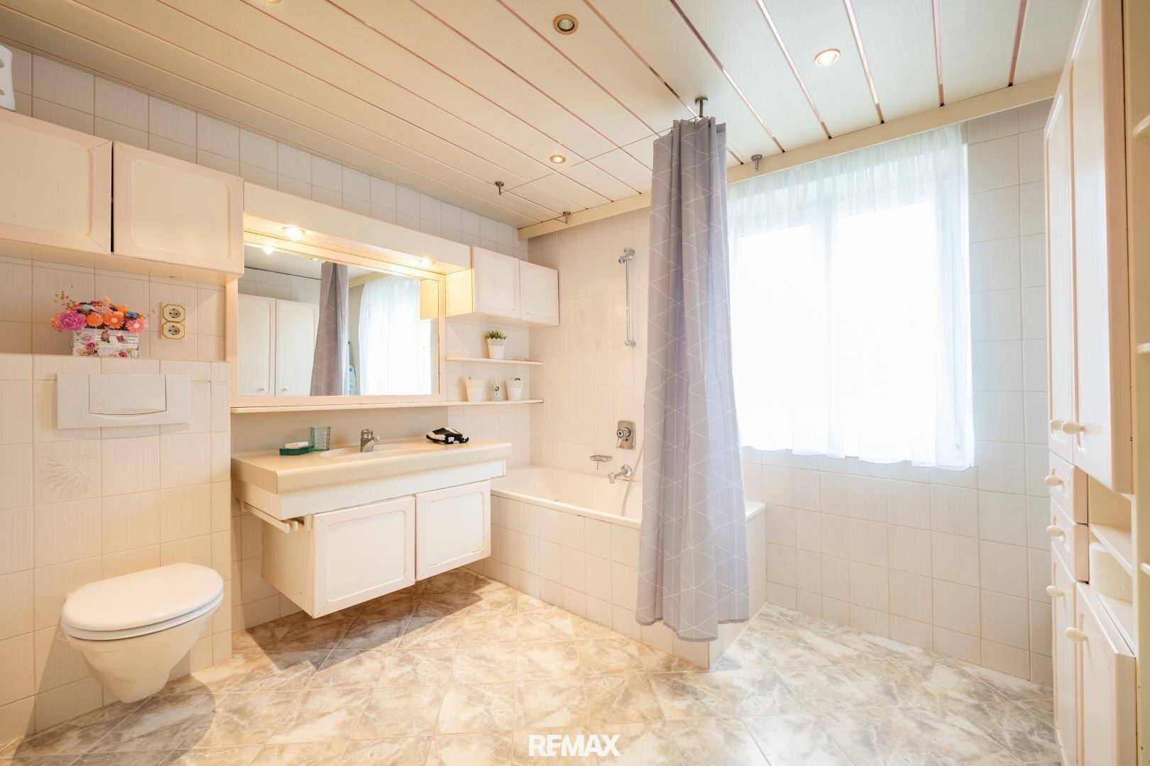 Funktionales Badezimmer mit Badewanne, Duschvorhang, Fenster und hellen Fliesen.