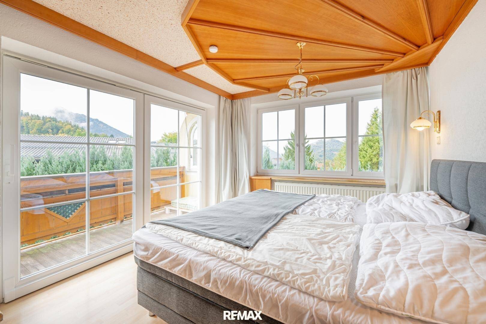 Helles Schlafzimmer mit Holzbalkendecke, großen Fenstern und Bergblick vom Balkon.