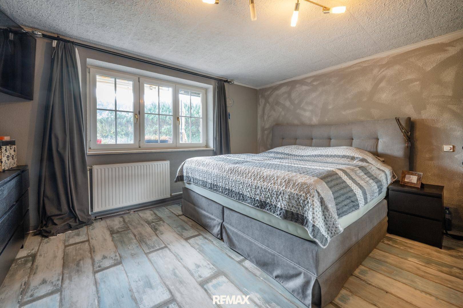 Schlafzimmer mit modernem Bett, Holzboden in Plankenoptik und Fenster.