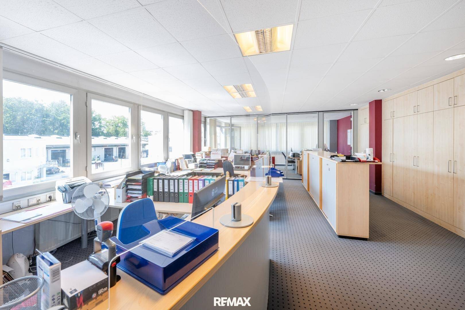 Helles und geräumiges Büro mit mehreren Arbeitsplätzen, Aktenschränken und großen Fenstern.