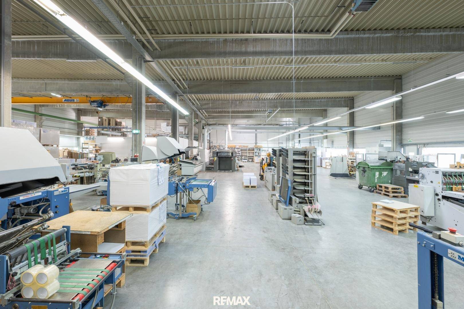 Geräumige Produktionshalle mit verschiedenen Maschinen, Paletten und guter Beleuchtung.