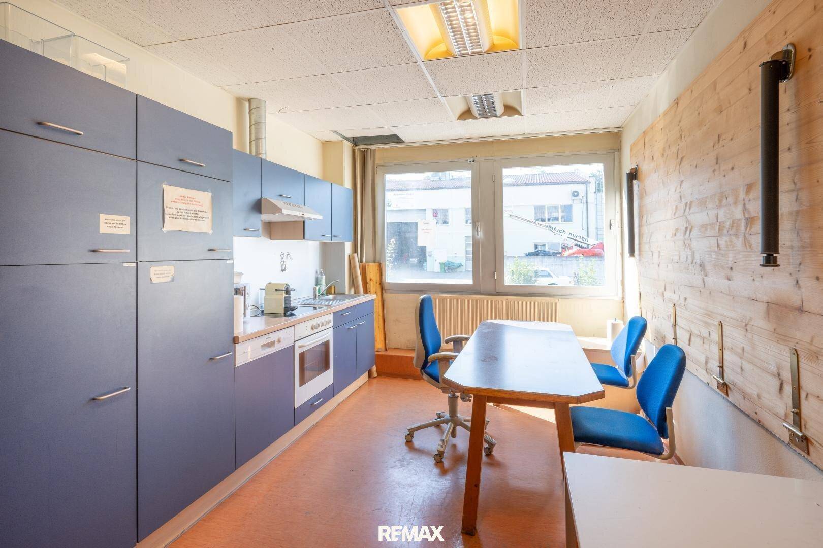 Funktionale Teeküche mit blauen Schränken, Esstisch und einem Fenster, ideal für Pausen.