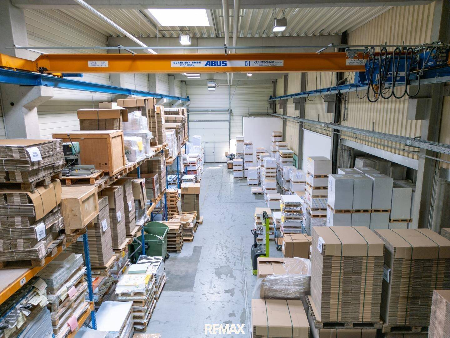 Lagerhalle mit hohen Decken, Regalen voller Kartons und einem gelben Brückenkran.