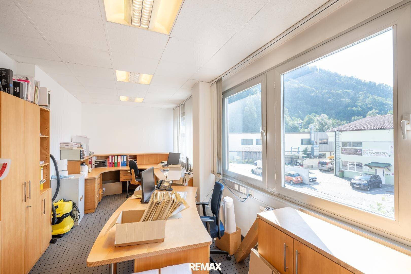 Helles Büro mit mehreren Arbeitsplätzen, Holzmöbeln und einem großen Fenster mit Bergblick.