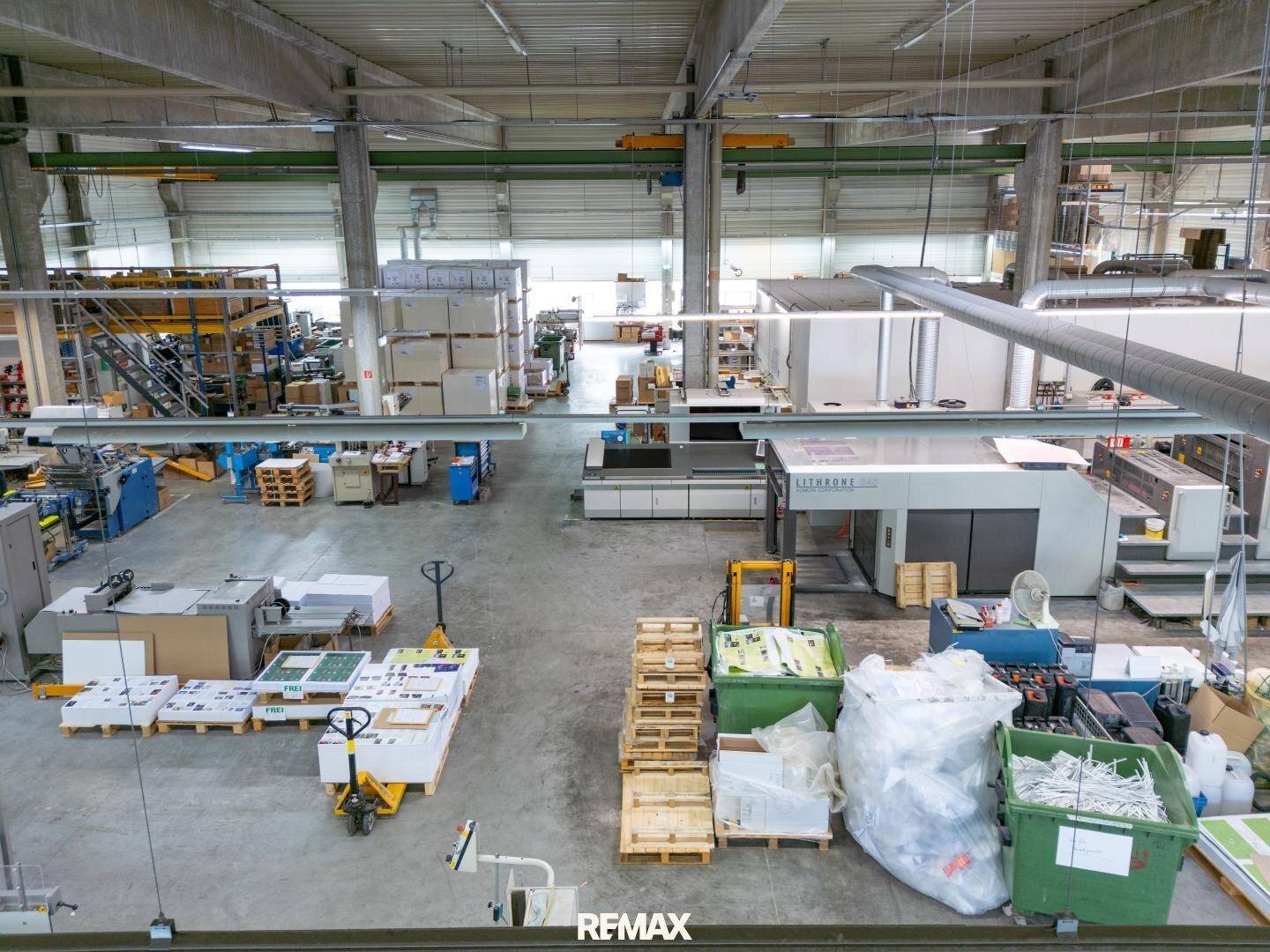 Große Produktionshalle mit Druckmaschinen, Paletten und hohen Decken, bereit für den Betrieb.