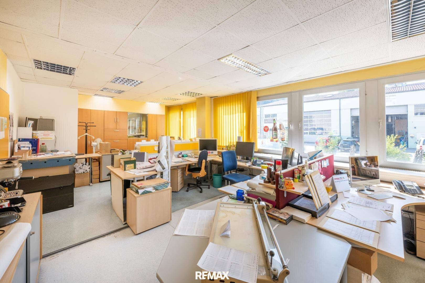 Großes Großraumbüro mit vielen Arbeitsplätzen, gelben Vorhängen und Blick auf die Umgebung.