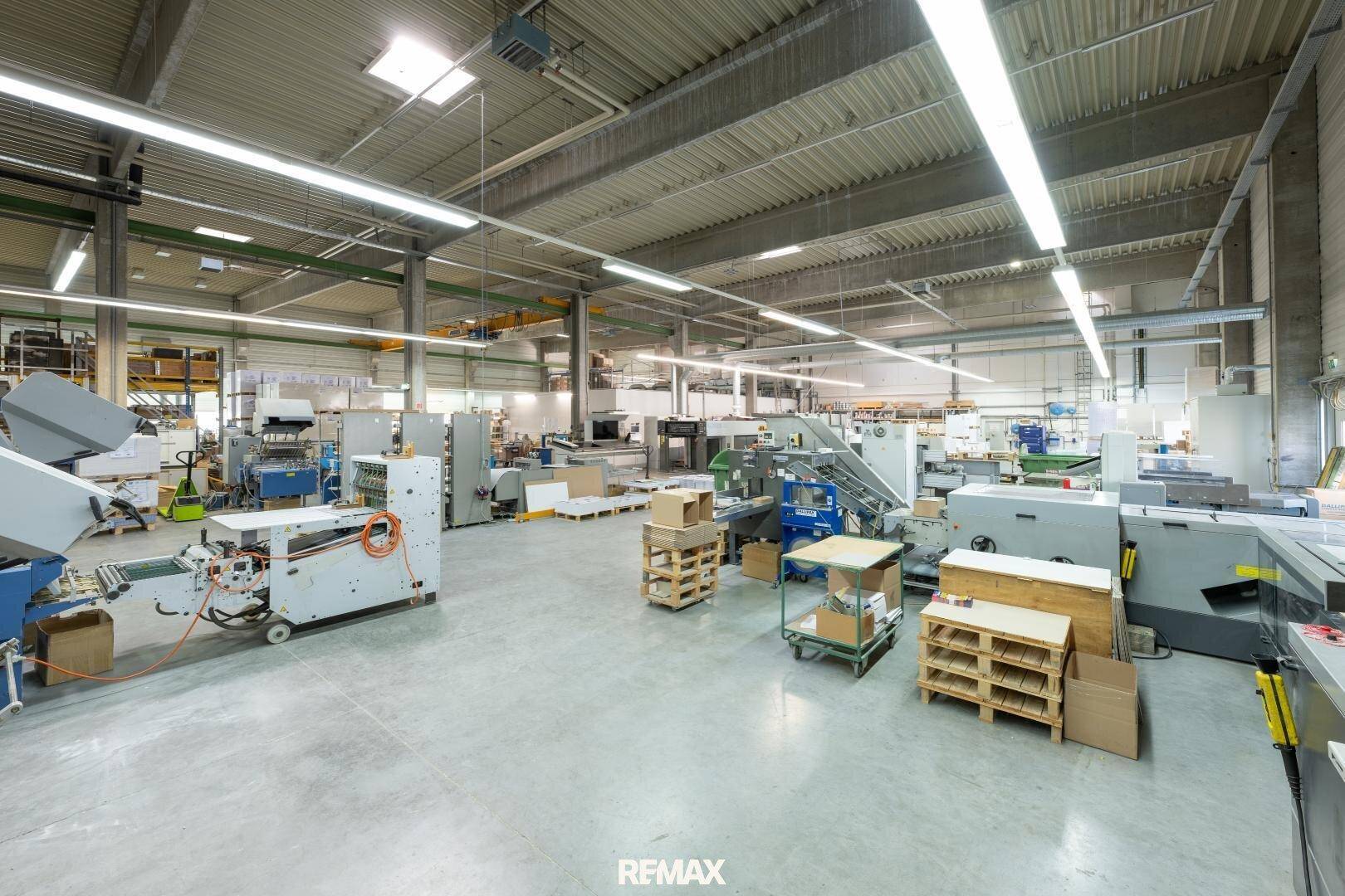 Weitläufige Produktionshalle mit verschiedenen Maschinen, glattem Betonboden und heller Beleuchtung.