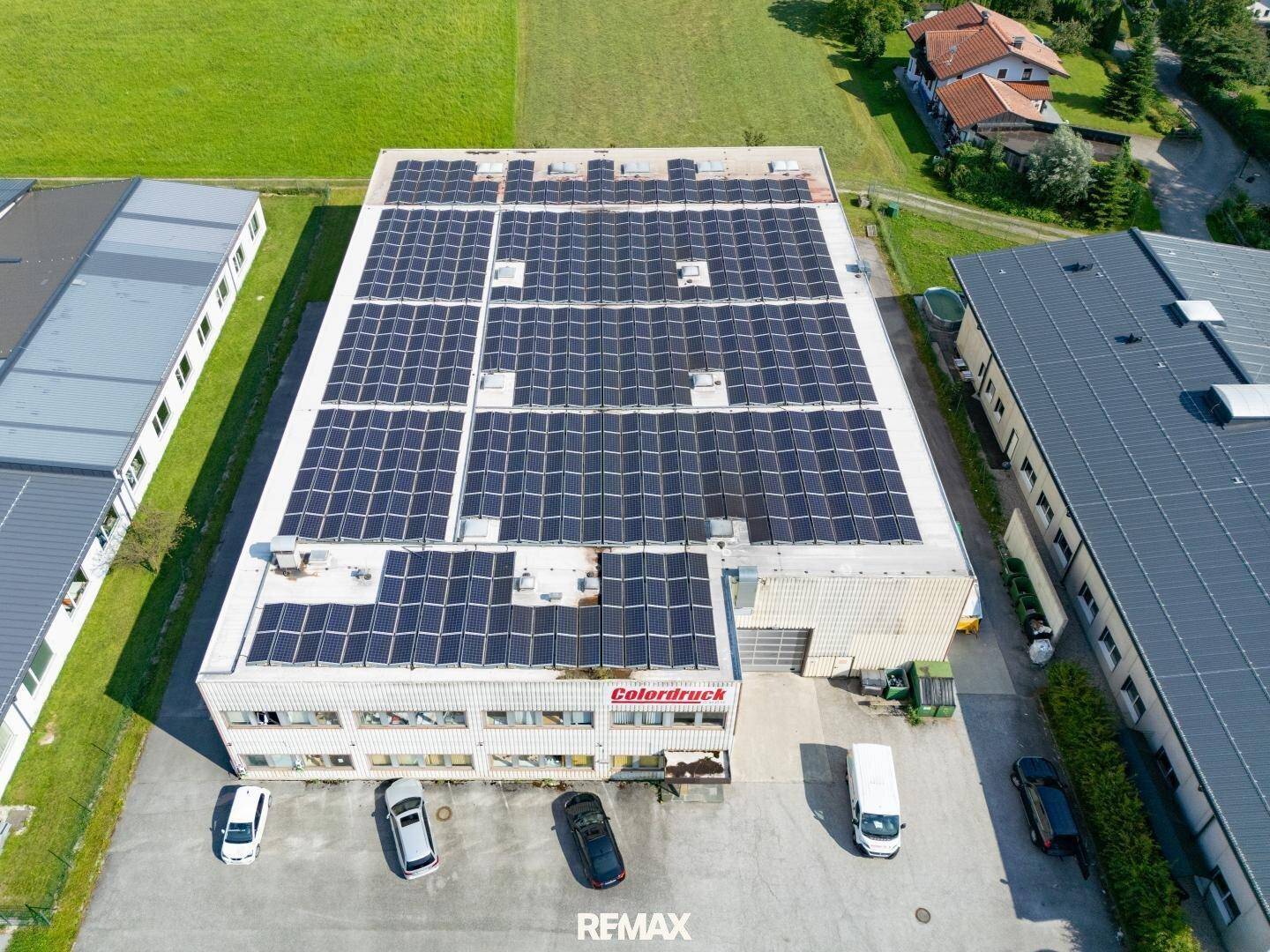 Übersichtliche Luftaufnahme des Gewerbegebäudes mit Solaranlage auf dem Dach und umliegender Landschaft.