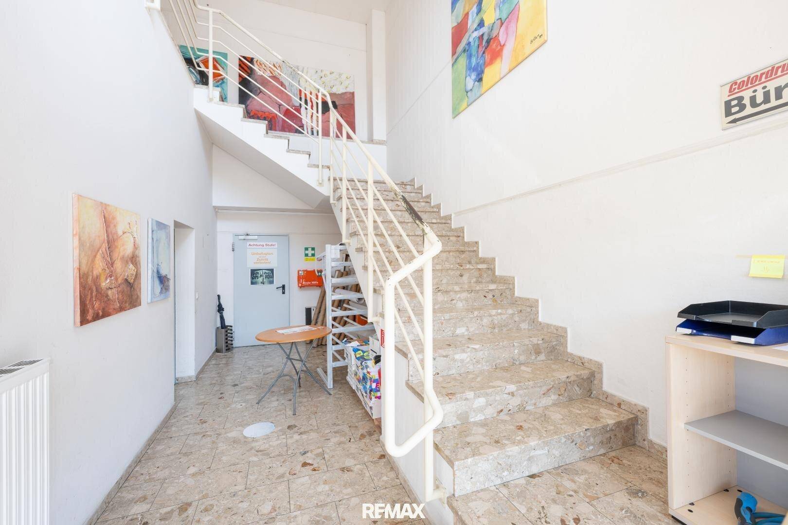 Heller Eingangsbereich mit Steintreppe, Fliesenboden und farbenfrohen Kunstwerken an den Wänden.