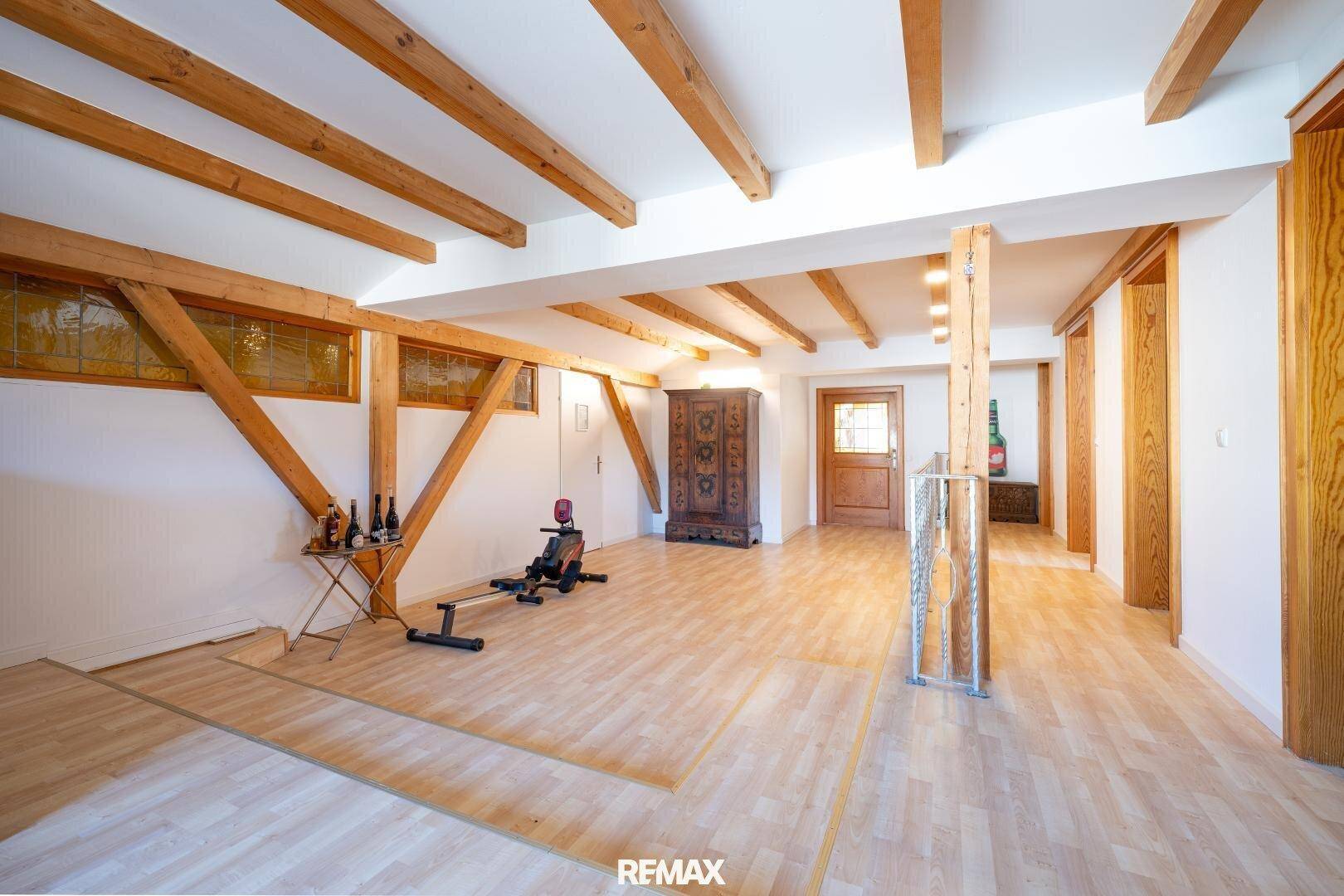 Geräumiger Raum mit sichtbaren Holzbalken, Holzboden und Fitnessgeräten.