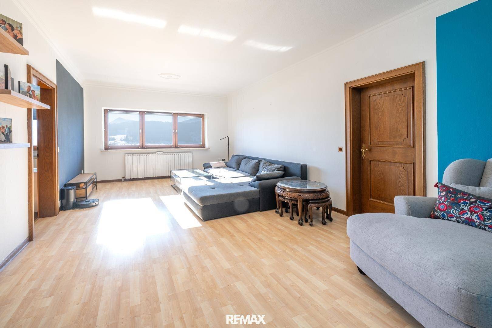 Helles Wohnzimmer mit großem Ecksofa, Holzboden und weitem Blick durch die Fenster.
