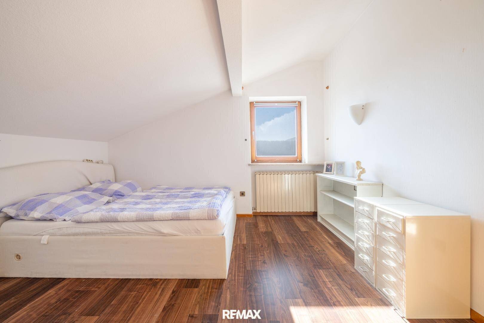 Helles Schlafzimmer im Dachgeschoss mit Holzboden, schräger Decke und modernem Mobiliar.