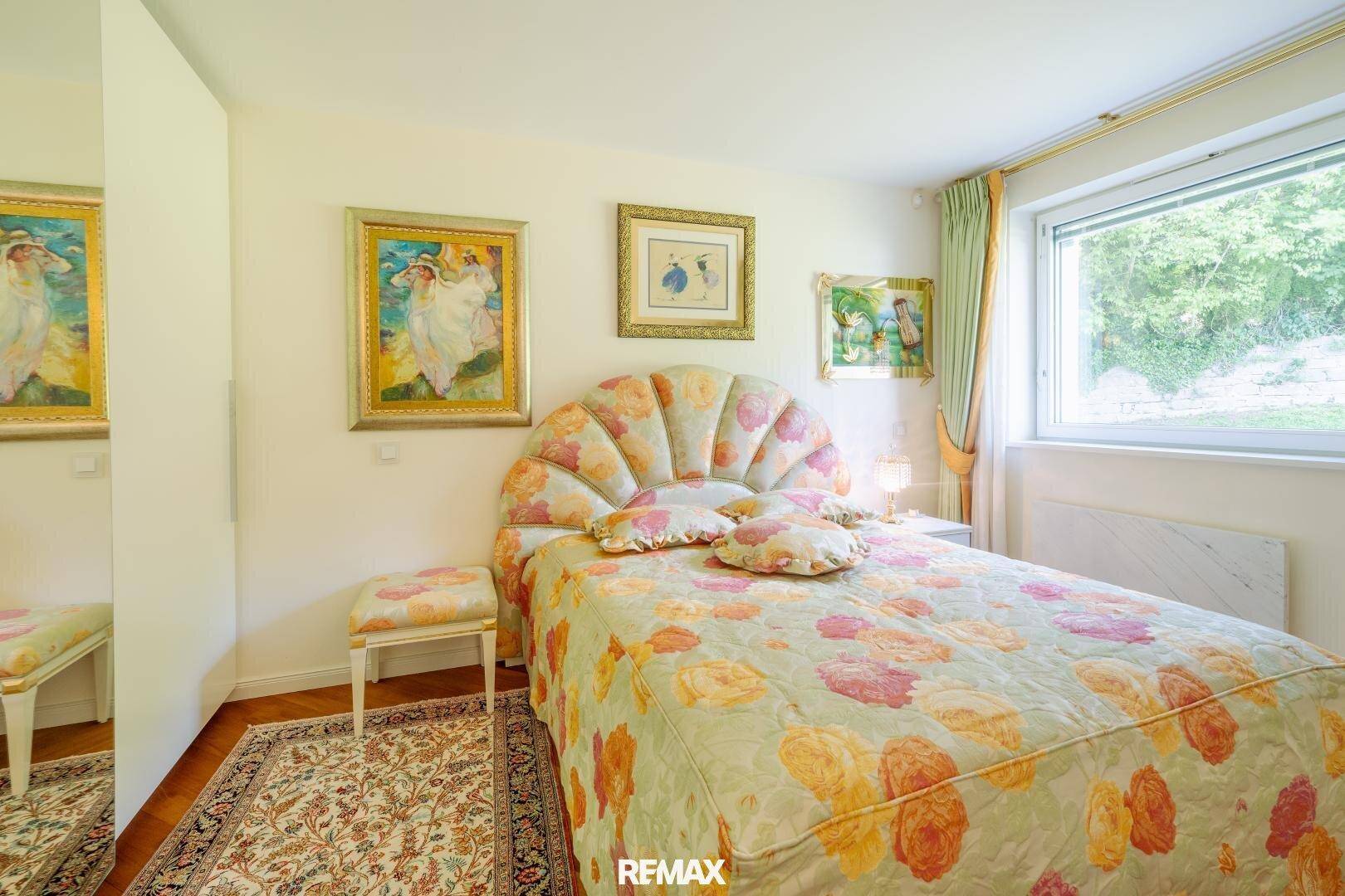 Gemütliches Schlafzimmer mit floraler Bettwäsche, Holzboden und Blick ins Grüne.