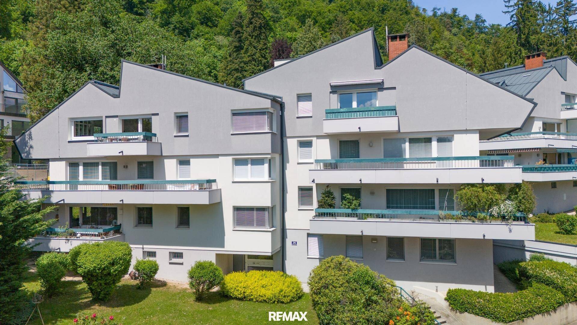 Mehrfamilienhaus mit moderner Architektur, Balkonen und grüner Umgebung.