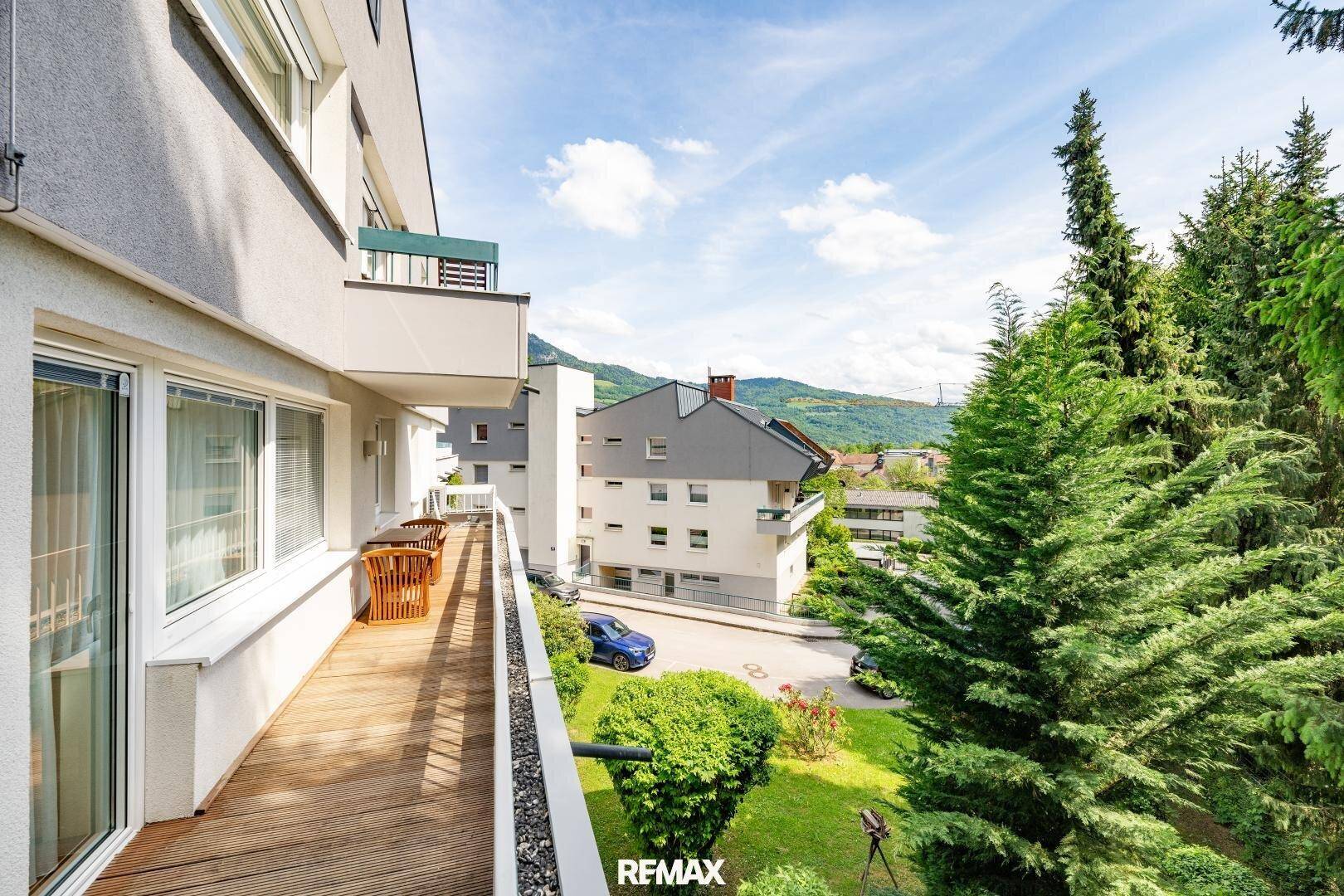 Langer Holzbalkon mit Sitzgelegenheiten und weitem Blick auf die grüne Landschaft.