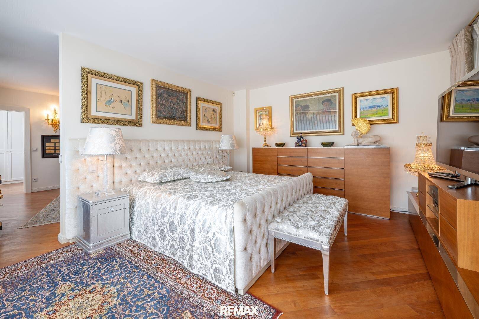 Luxuriöses Schlafzimmer mit gepolstertem Bett, Holzboden und vielen Kunstwerken.