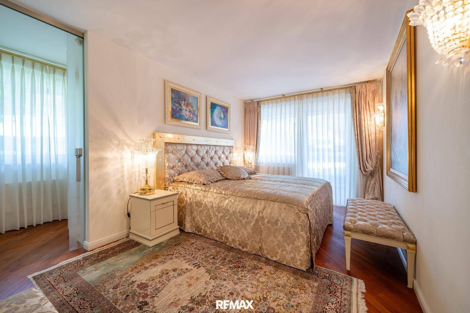 Helles Schlafzimmer mit großem Bett, Holzboden und Zugang zu einem weiteren Raum.