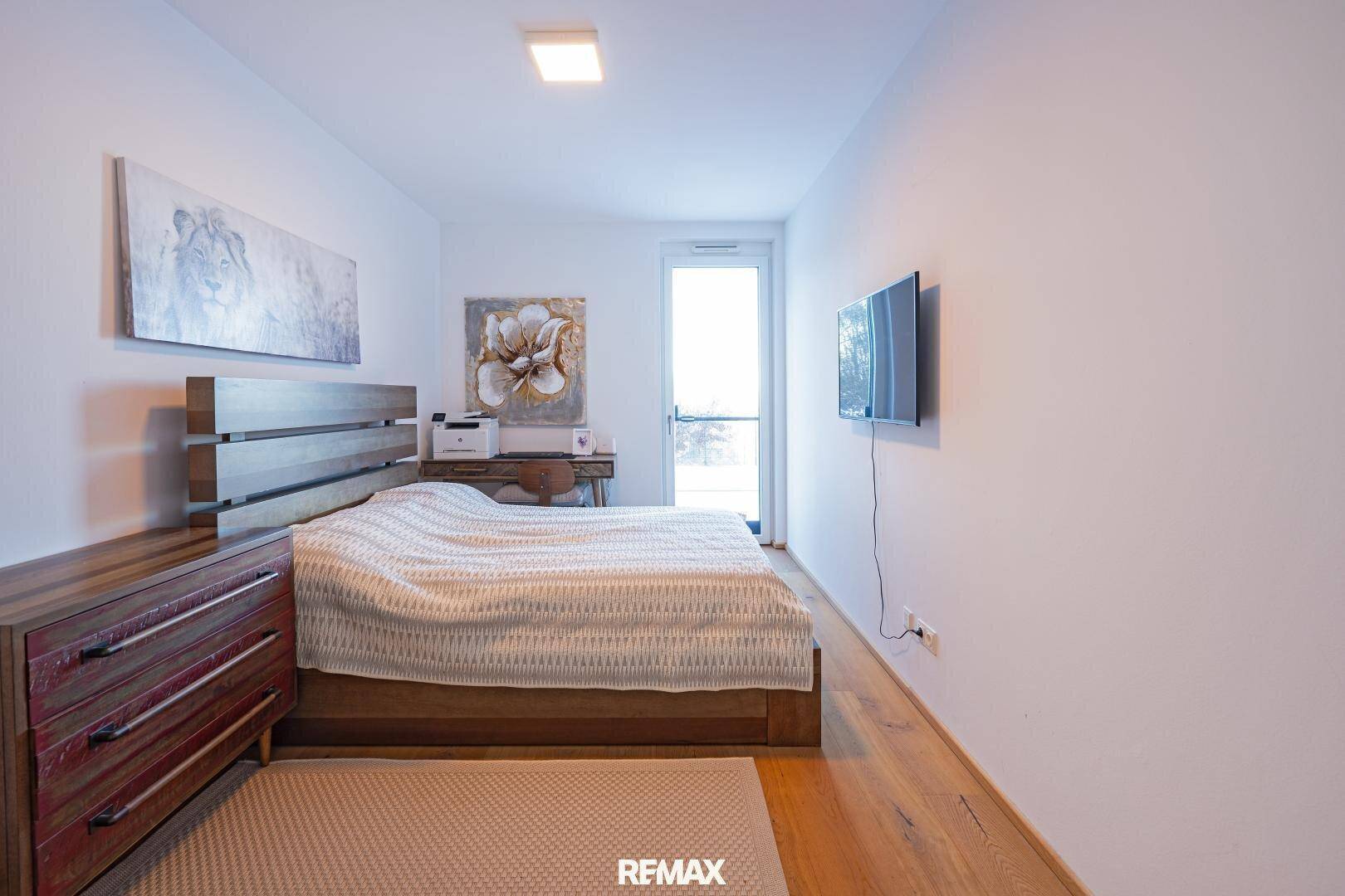Gemütliches Schlafzimmer mit Holzboden, Holzbett und einem Schreibtischbereich am Fenster.