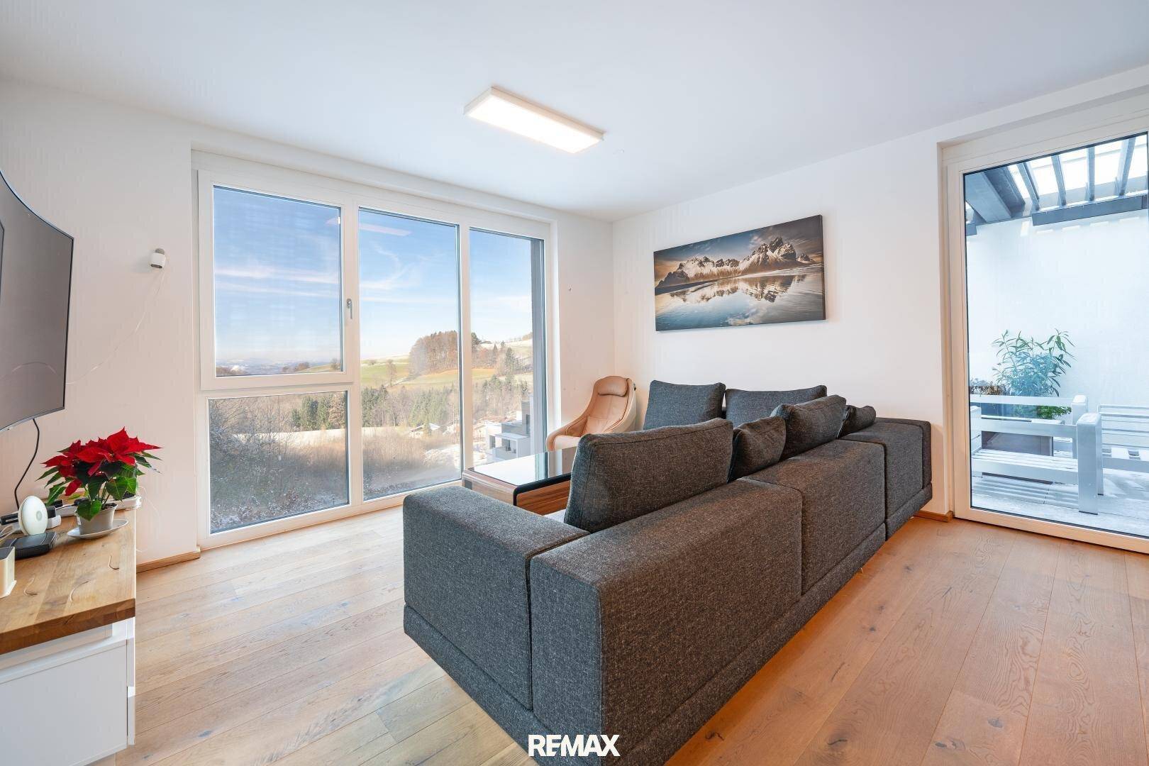 Helles Wohnzimmer mit Holzboden, großem Sofa und Zugang zu einem Balkon mit Weitblick.