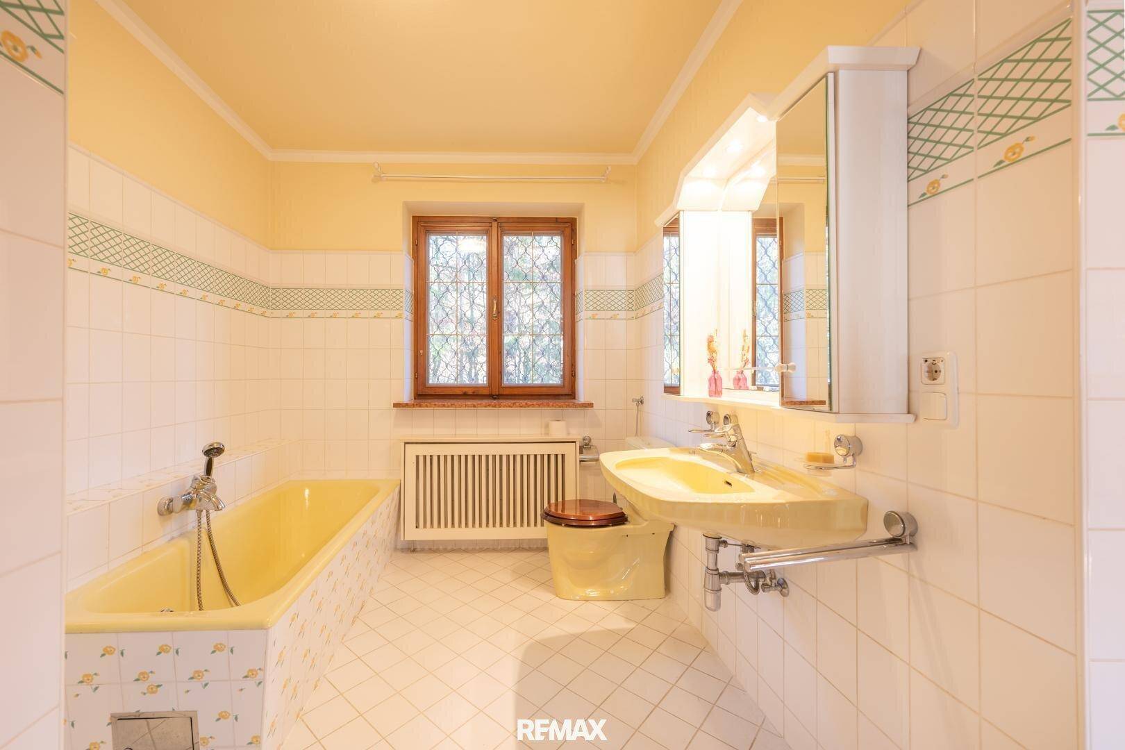 Badezimmer im 80er-Jahre-Stil mit gelber Badewanne, Waschbecken und Fliesen.